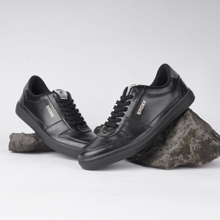 Stylish black sneakers posed elegantly on rocks, showcasing contemporary fashion footwear.